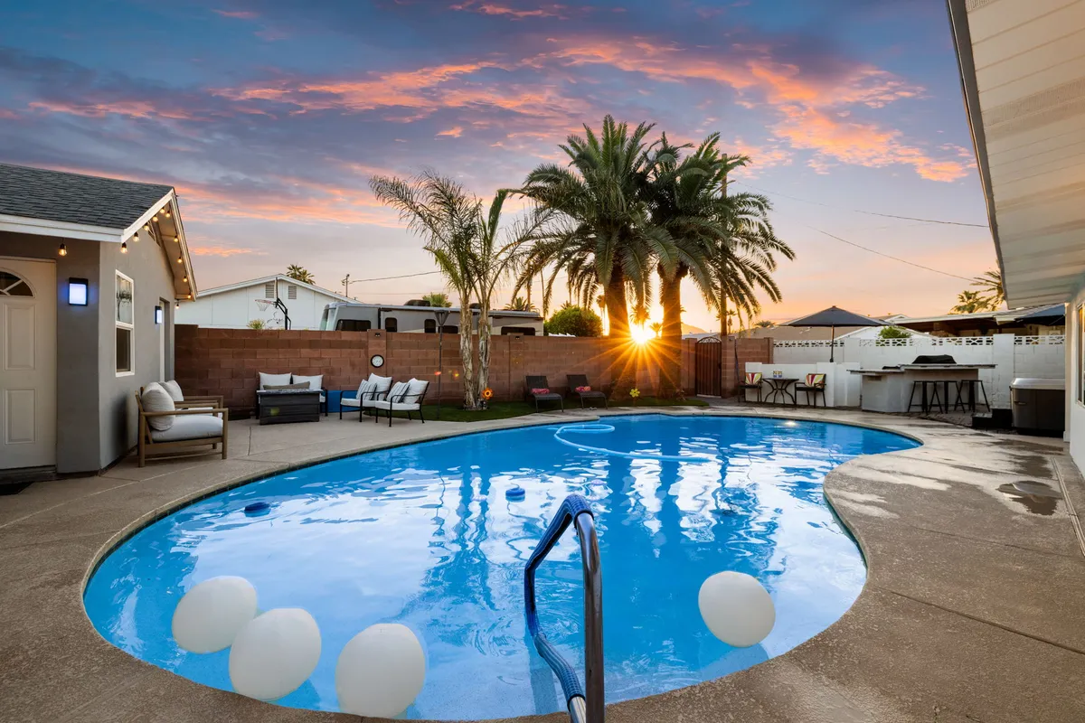 An exterior scene featuring a sparkling swimming pool surrounded by palm trees and a stylish outdoor seating area at sunset. The tranquil yet lively setting is perfect for informal team gatherings, relaxation, or after-hours networking.