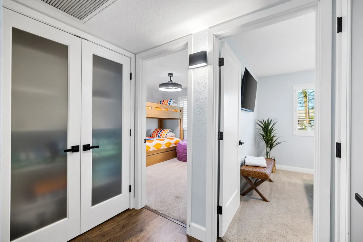 A playful, colorful kids' room featuring bunk beds with bright bedding, a soft area rug, a decorative plant, and modern lighting. The space feels cozy and cheerful, perfect for children to relax or play games.
