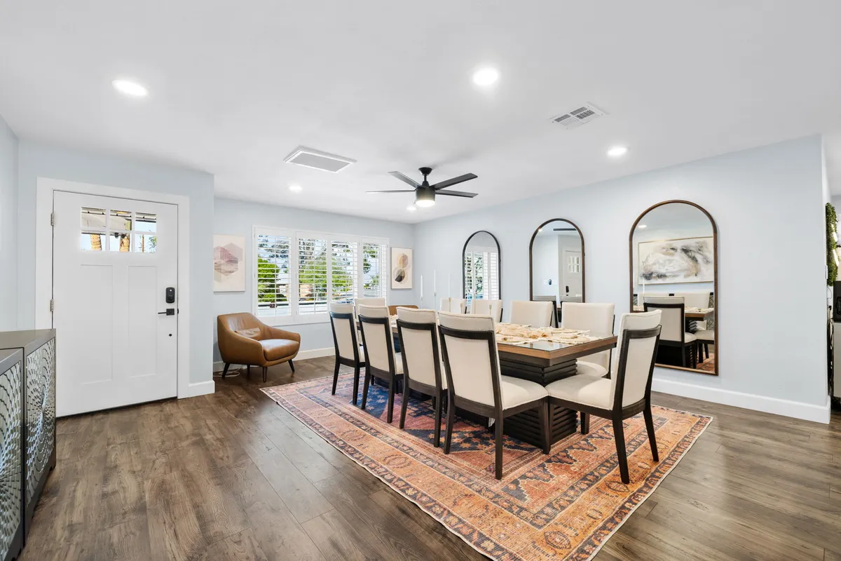 A large dining table sits under elegant chandeliers, surrounded by mirrors and a stylish rug, with the entryway door visible in the background. The setting is perfect for family dinners, group celebrations, or festive gatherings, embodying a sense of togetherness.
