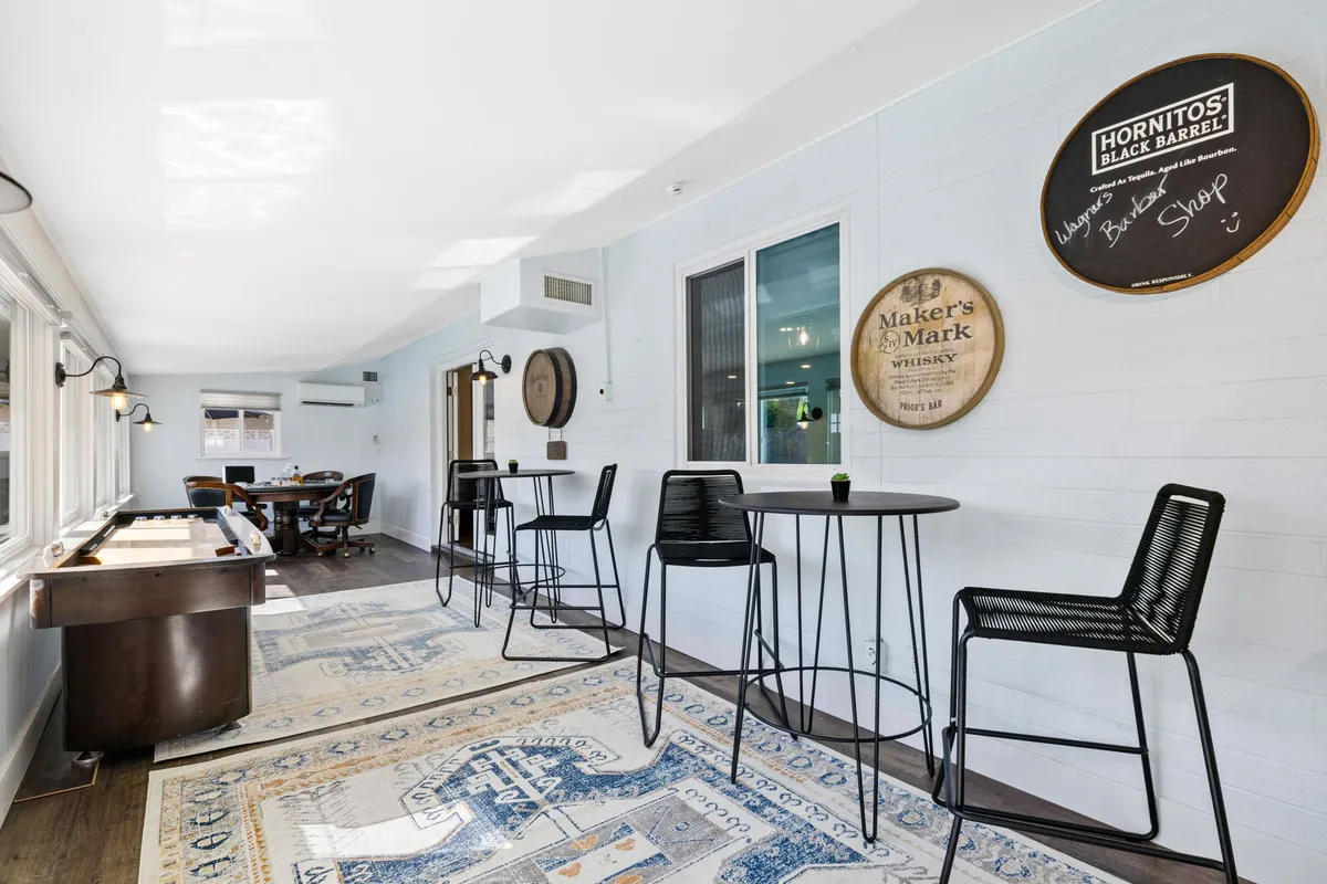 A stylish interior game room featuring bar stools, a pool table, decorative wall signs, and a relaxed seating area with a cozy rug. The space is designed for casual gatherings and fun group activities like playing pool and enjoying drinks.