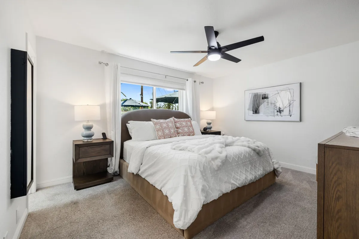 A tranquil and cozy bedroom featuring a neatly made bed with decorative pillows, a window allowing in natural light, and a nightstand with a lamp. The space feels warm and inviting, perfect for unwinding and relaxation.