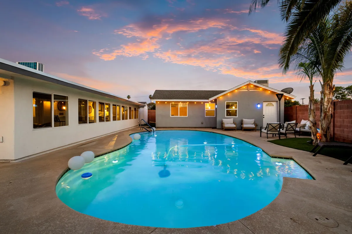 A vibrant outdoor setting with a shimmering pool, palm trees, comfortable seating, and a sky painted with sunset colors. It exudes an atmosphere of welcoming relaxation, perfect for social gatherings or winding down after an evening out.