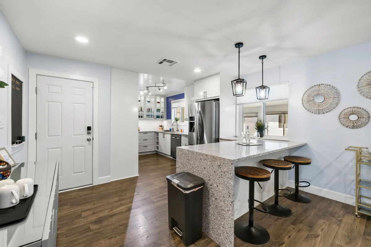 A bright kitchen with a central island fitted with bar stools, pendant lights, and visible kitchen appliances. The open design makes it easy to gather around the island for casual dining, conversation, or meal prep, promoting togetherness and interactive cooking experiences.